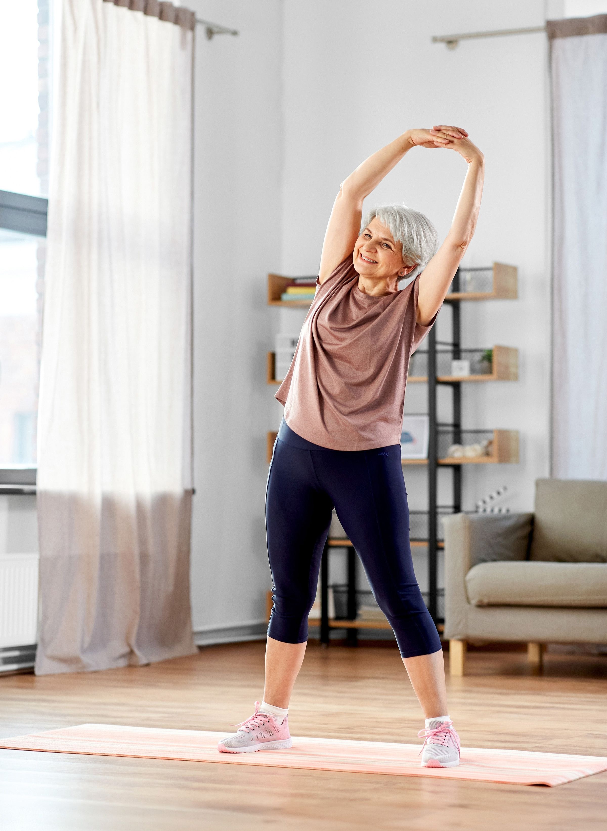 Photo of a woman in workout clothes stretching indoors at her home
