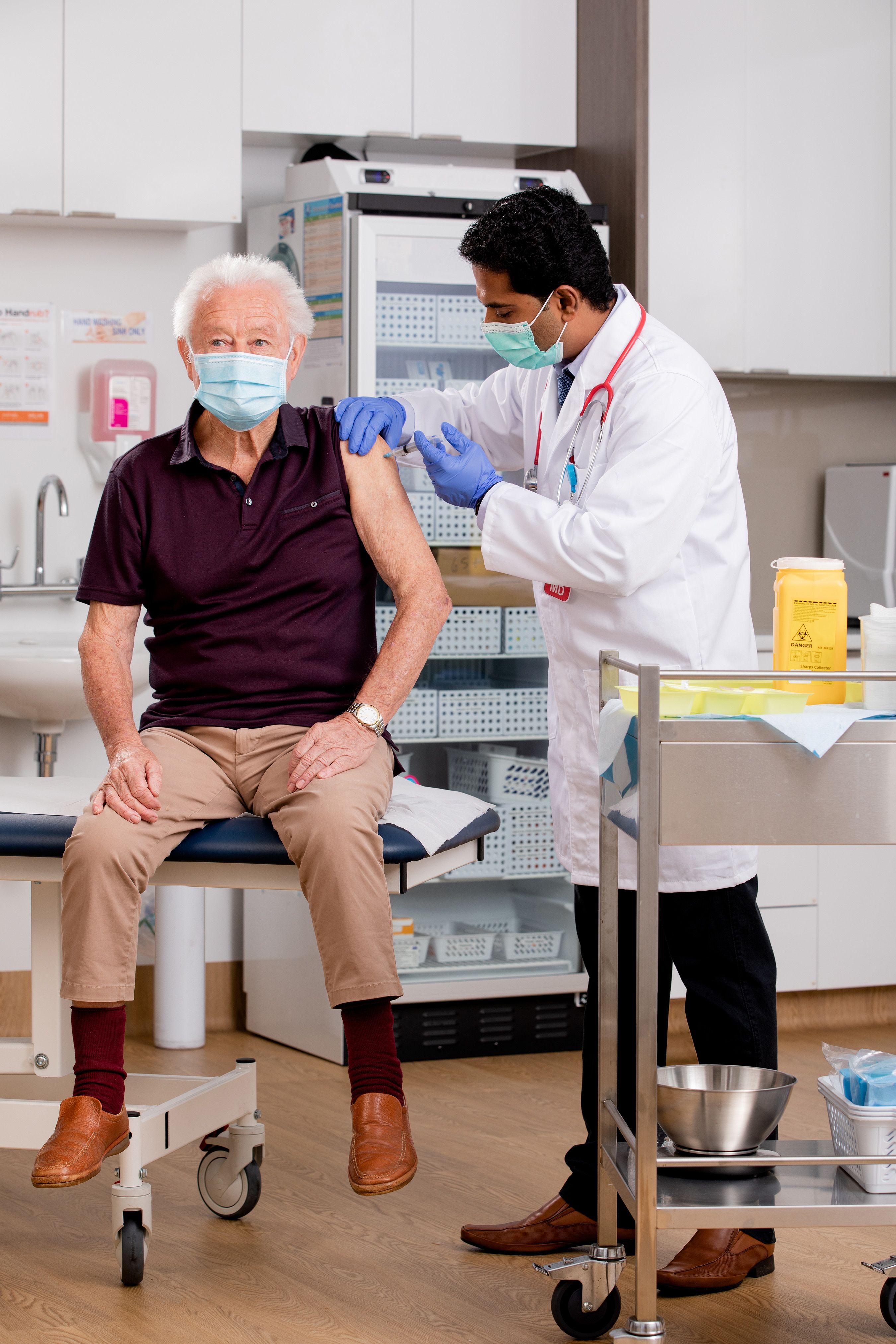Photo of an elderly man at a clinic receiving a vaccination in his arm. 