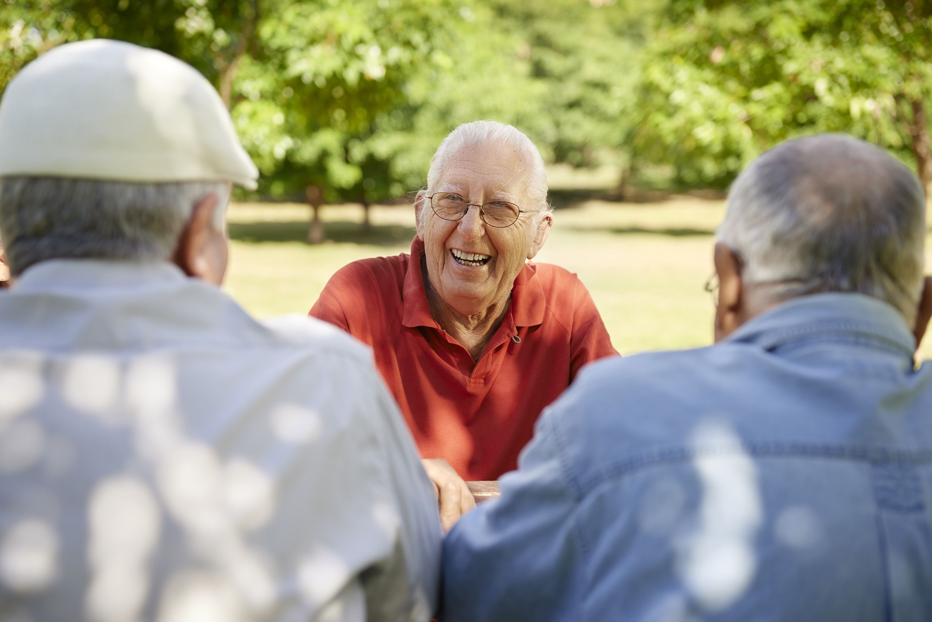 Photo of three elderly man talking and playing cards at a park