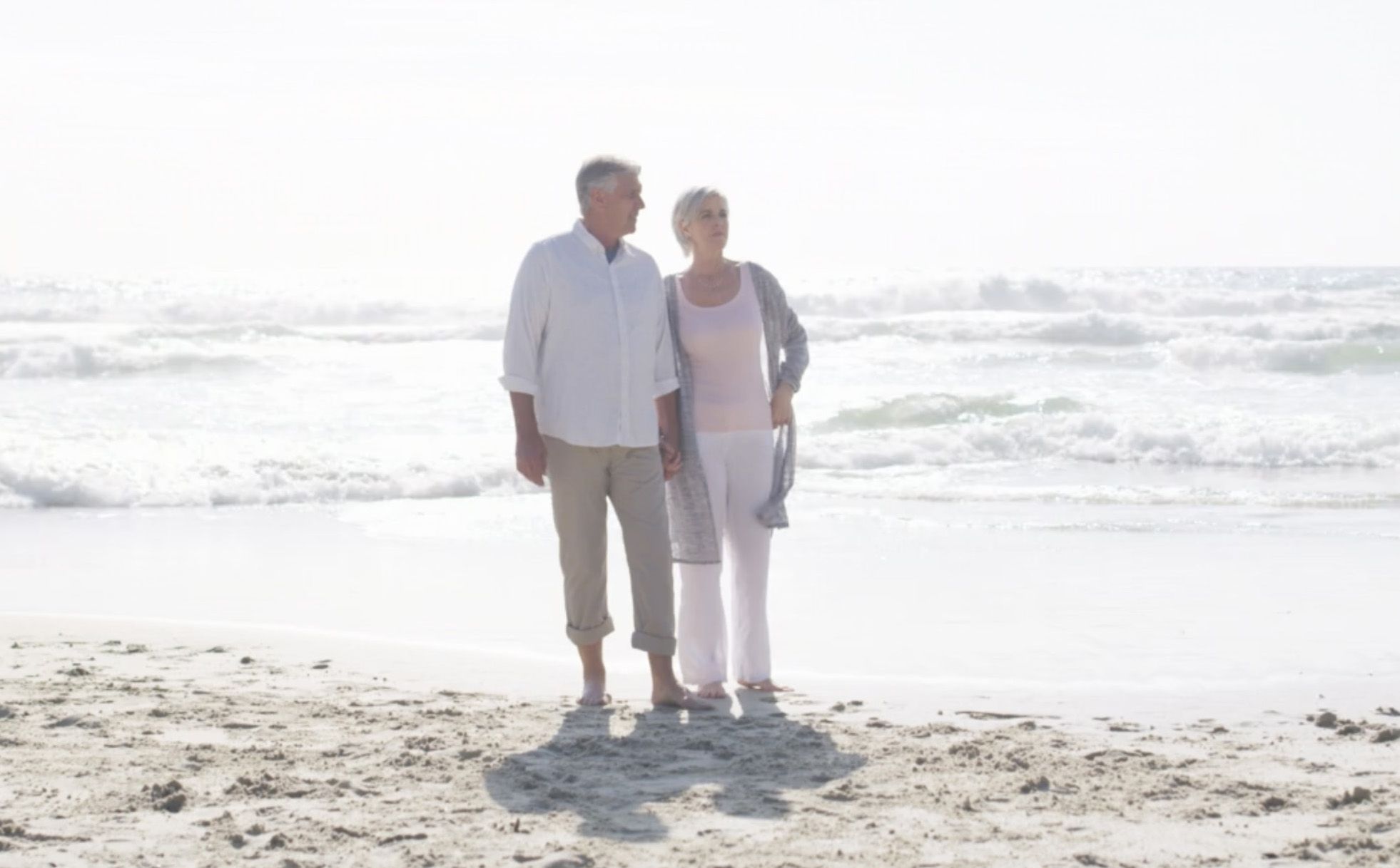 Photo of a man an woman walking along a sunny beach